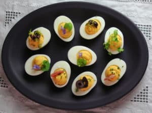 Assorted deviled eggs on dark purple plate.